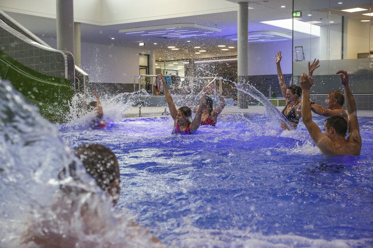 Mehrere Menschen im Nichtschwimmerbecken, Wasser spritzt, links im Bild eine Rutsche