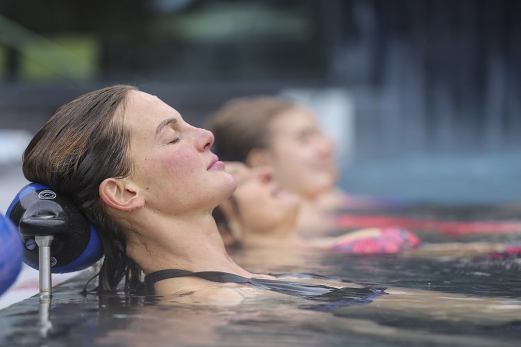 Badende, die im Außenbecken auf Kopfstützen im Wasser entspannen