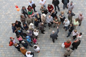 Das Foto zeigt von oben herabfotografiert eine Gruppe von Menschen, die um einen Stadtführer gesammel stehen und offenbar interessiert zuhören.