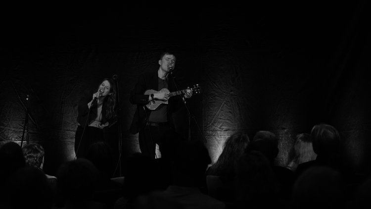 schwarz-weiß Foto mit einer Sängerin und einem Sänger mit Ukulele auf der Bühne