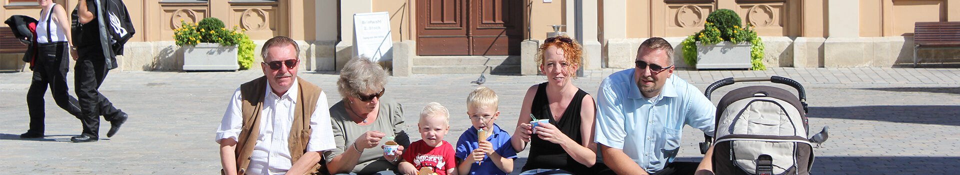 Eine Familie, Eltern, Kinder und Großeltern mit einem Kinderwagen vor dem Rathaus