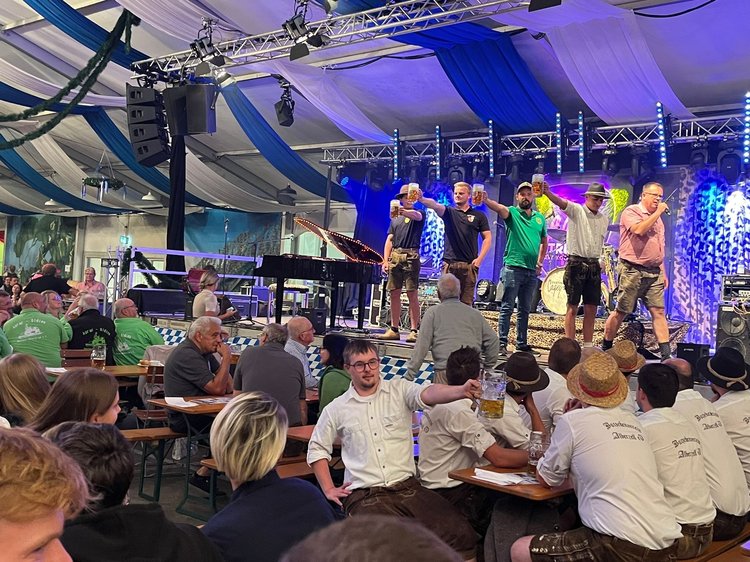 Volksfest im Zelt, auf der Bühne Menschen beim Maßkrug-Stemmen