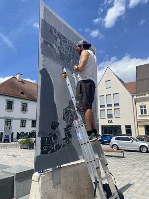 Mann steht auf einer Leiter und kreiert ein Bild auf dem Hautplatz