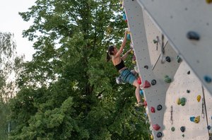 Kletterin an einer Boulder-Wand, im Hintergrund Bäume