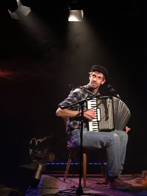 Maxi Pongratz mit Akkordeon sitzend auf einer dunklen Bühne