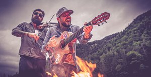 Zwei Männer mit Geige und Gitarre in der Natur und Lagerfeuer
