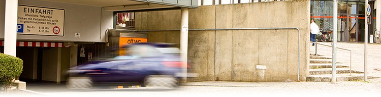 Einfahrt zur Parkgarage mit einem Auto, das gerade auf die Rampe fährt.